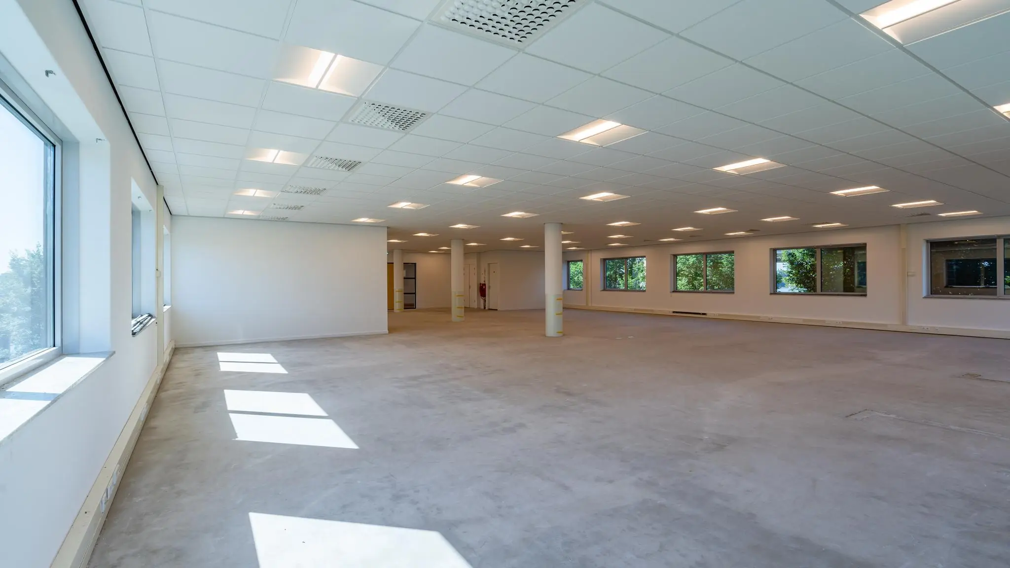 Leeg en licht kantoorruimte-interieur aan de Rivium Promenade met grote ramen en systeemplafond.